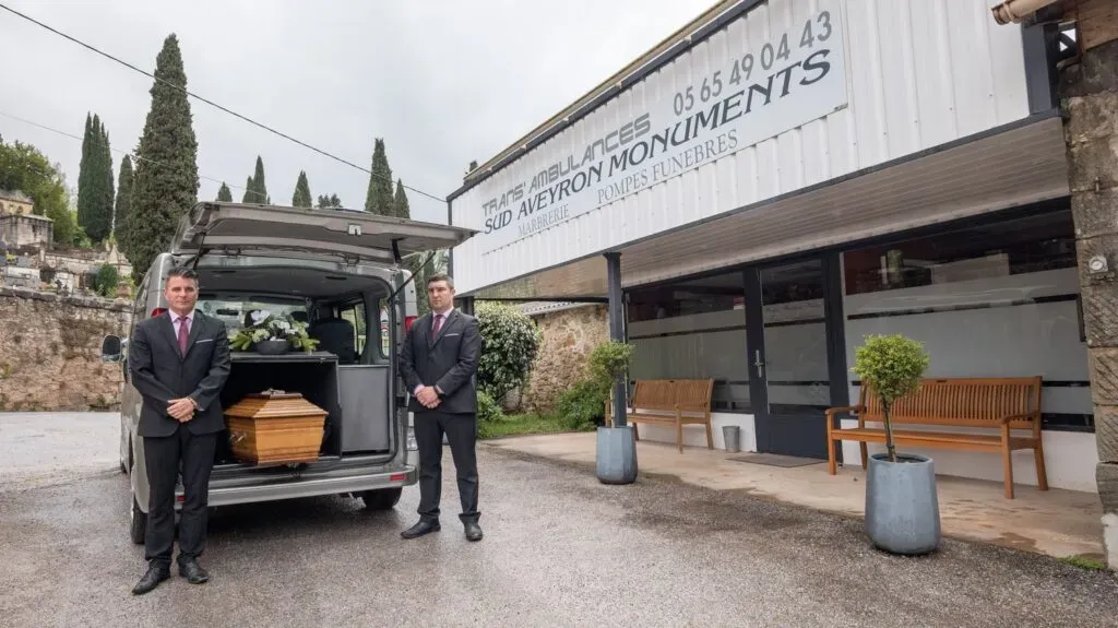 Véhicule funéraire et porteurs devant l'agence Sud Aveyron Monuments.